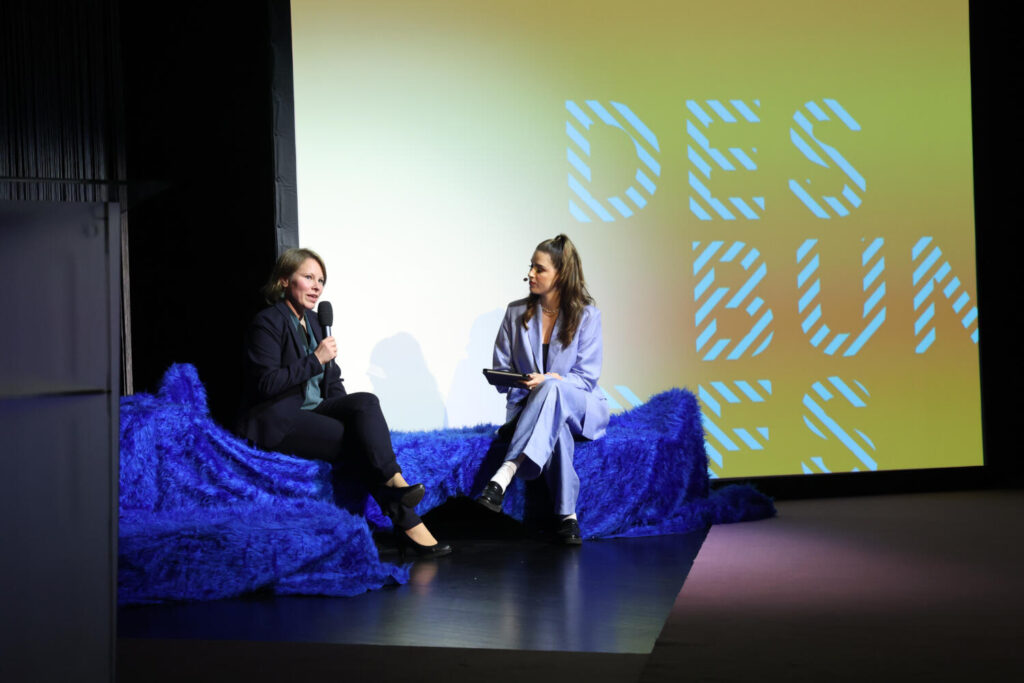 Theresa Schütz and Salwa Houmsi sit on a blue plush landscape and chat.