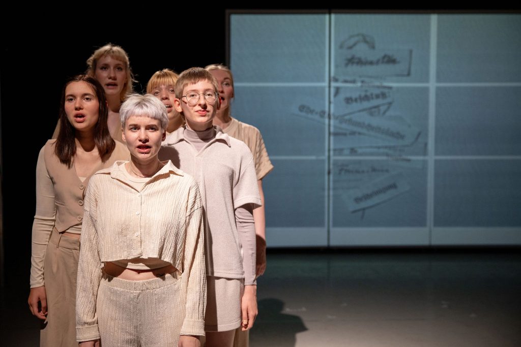 Scene from “Erased”: Six people stand close together on stage.