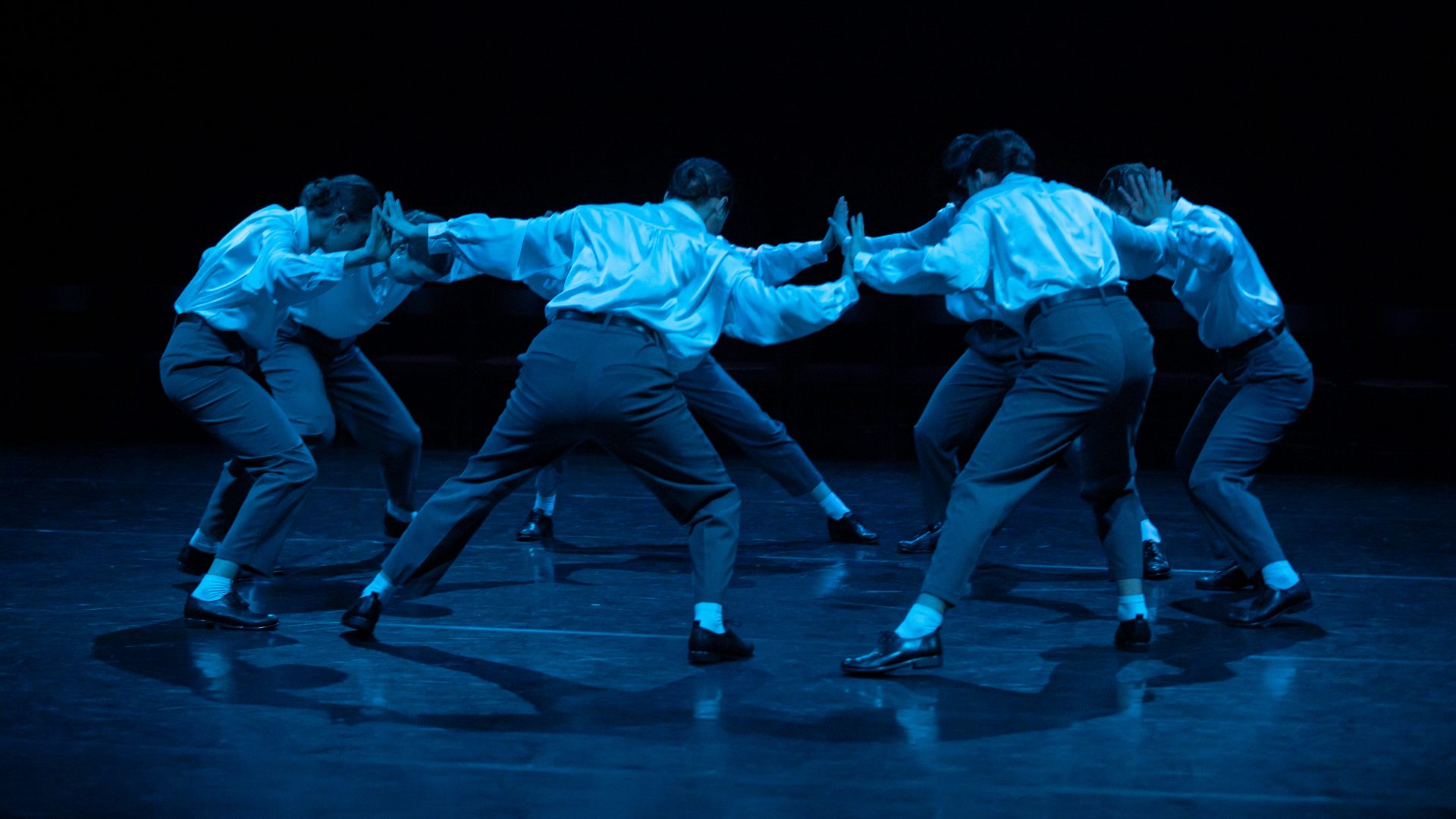 Szene aus "Ring": In blaues Licht getaucht bilden Tänzer*innen einen Kreis, stützen sich gegenseitig.