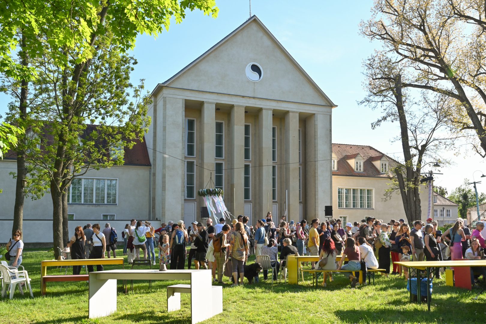 Außenaufnahme des Festpsielhauses in HELLERAU mit einer großen Publikumsmenge bei sonnigem Wetter.