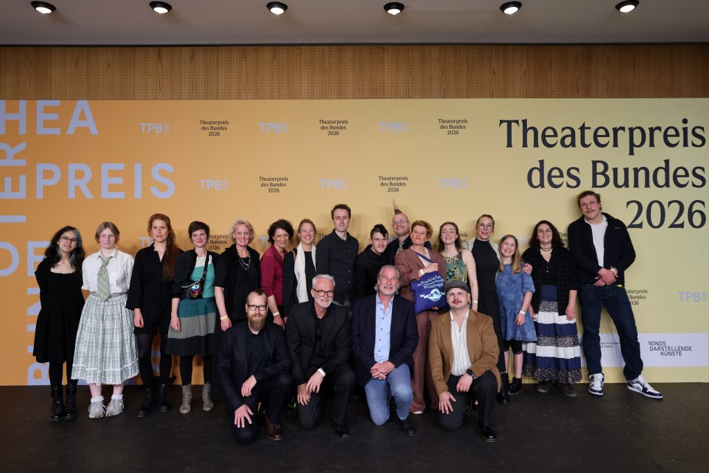 Das Team steht vor einer Fotowand mit dem Aufdruck: Theaterpreis des Bundes 2026.