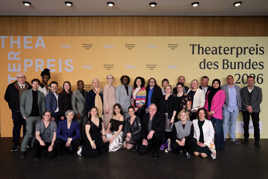 Das Team steht vor einer Fotowand mit dem Aufdruck: Theaterpreis des Bundes 2026.