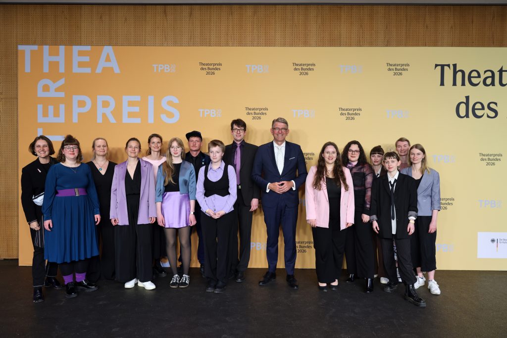 Das Team steht gemeinsam mit dem Staatsminister vor einer Fotowand mit dem Aufdruck: Theaterpreis des Bundes 2026.