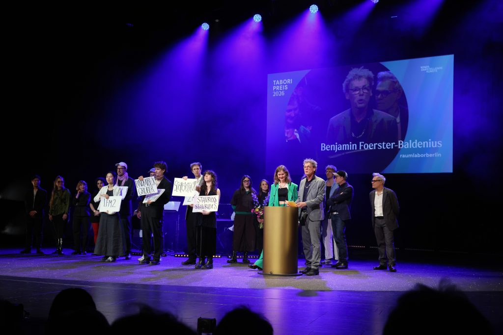 Benjamin und Anna Foerster-Baldenius am Pult. Das Team dahinter hält Pappen mit Namen von Theatergruppen hoch.