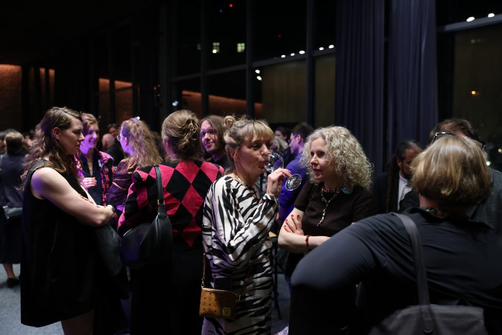 Menschen stehen im Foyer, reden miteinander und halten Getränke in den Händen.